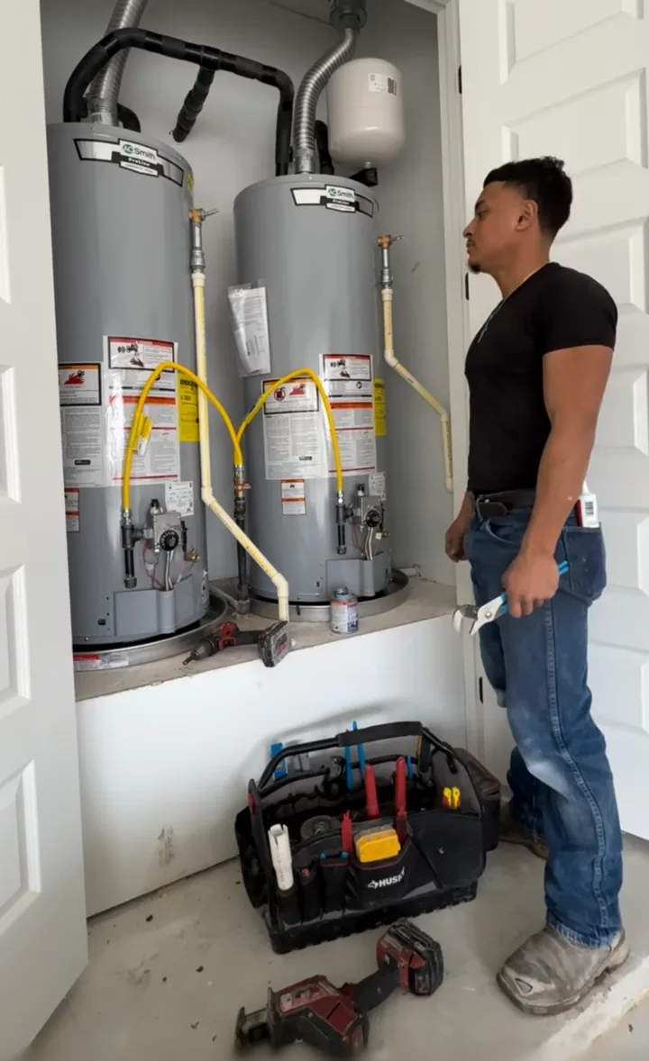 Christian standing in front of two water heaters with a pair of pliers and a tool bag at his feet
